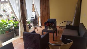 A patio area with wicker furniture, a table with a vase of flowers, and potted plants.