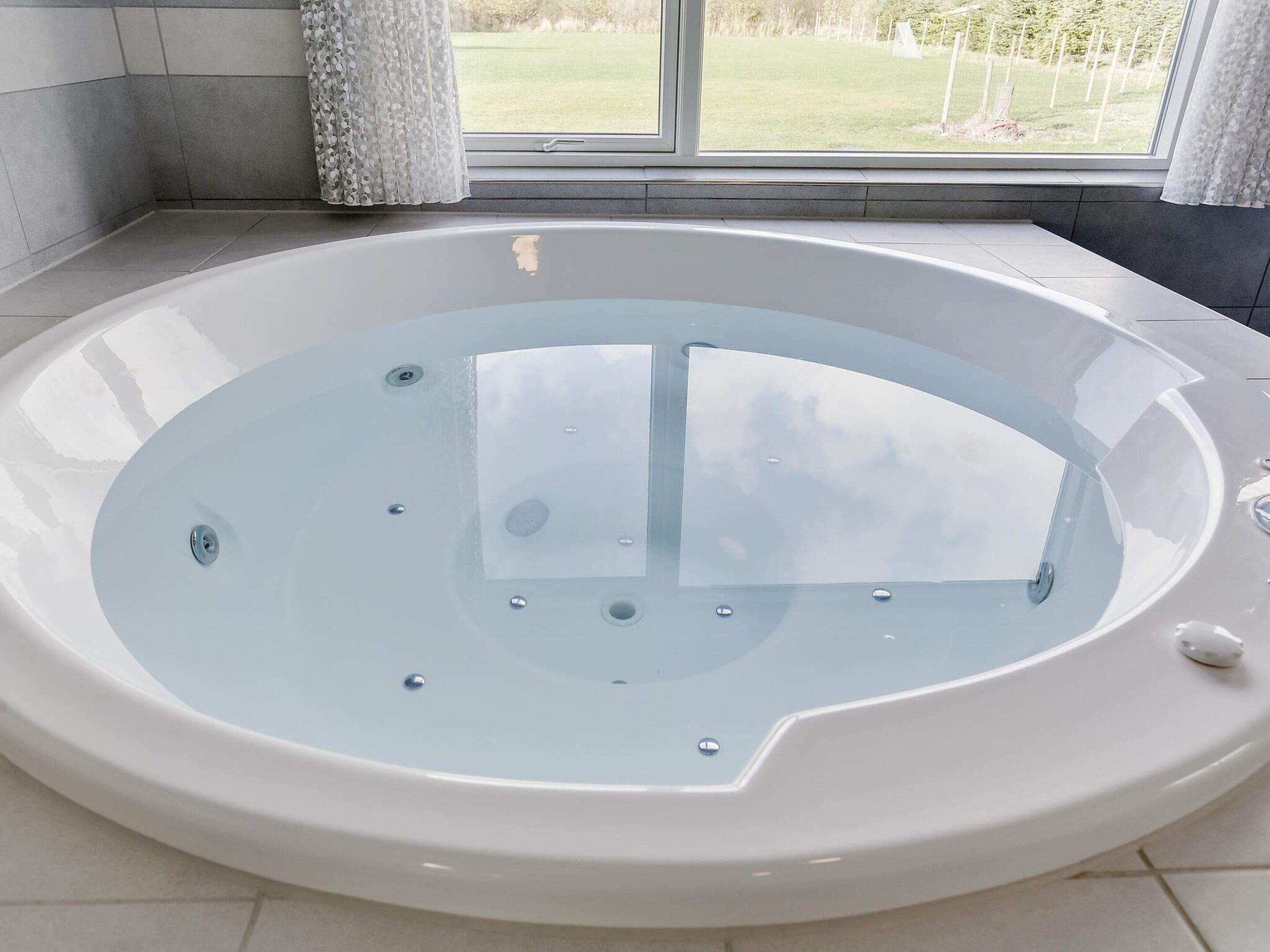 A modern bathroom with a freestanding bathtub, a window with a view of a grassy area, and a tiled floor.