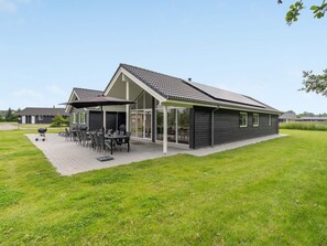 A modern building with a covered patio area, outdoor seating, and a barbecue grill.