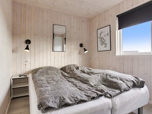 A bedroom with a bed, bedside tables, a mirror, wall-mounted lamps, and a window with a view.