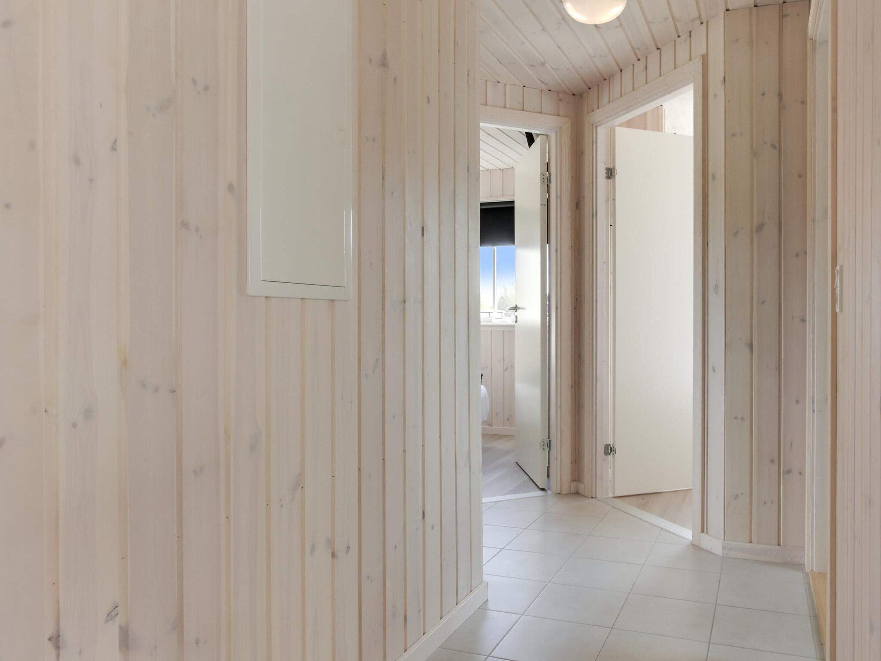 A hallway with wooden paneling and a tiled floor, leading to a room with a door.
