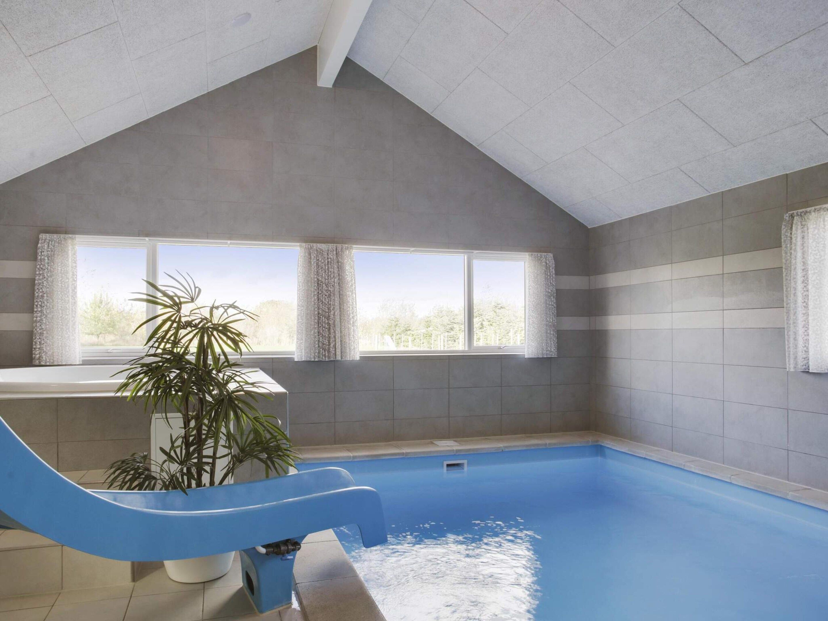 A swimming pool with a blue slide, a potted plant, and a view of trees through the windows.