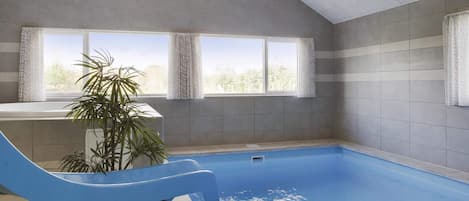 A swimming pool with a blue slide, a potted plant, and a view of trees through the windows.