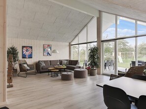 A spacious living room with a large window, a sofa, a coffee table, and a dining area. - 5 Star Holiday Home in Idestrup (Idestrup)