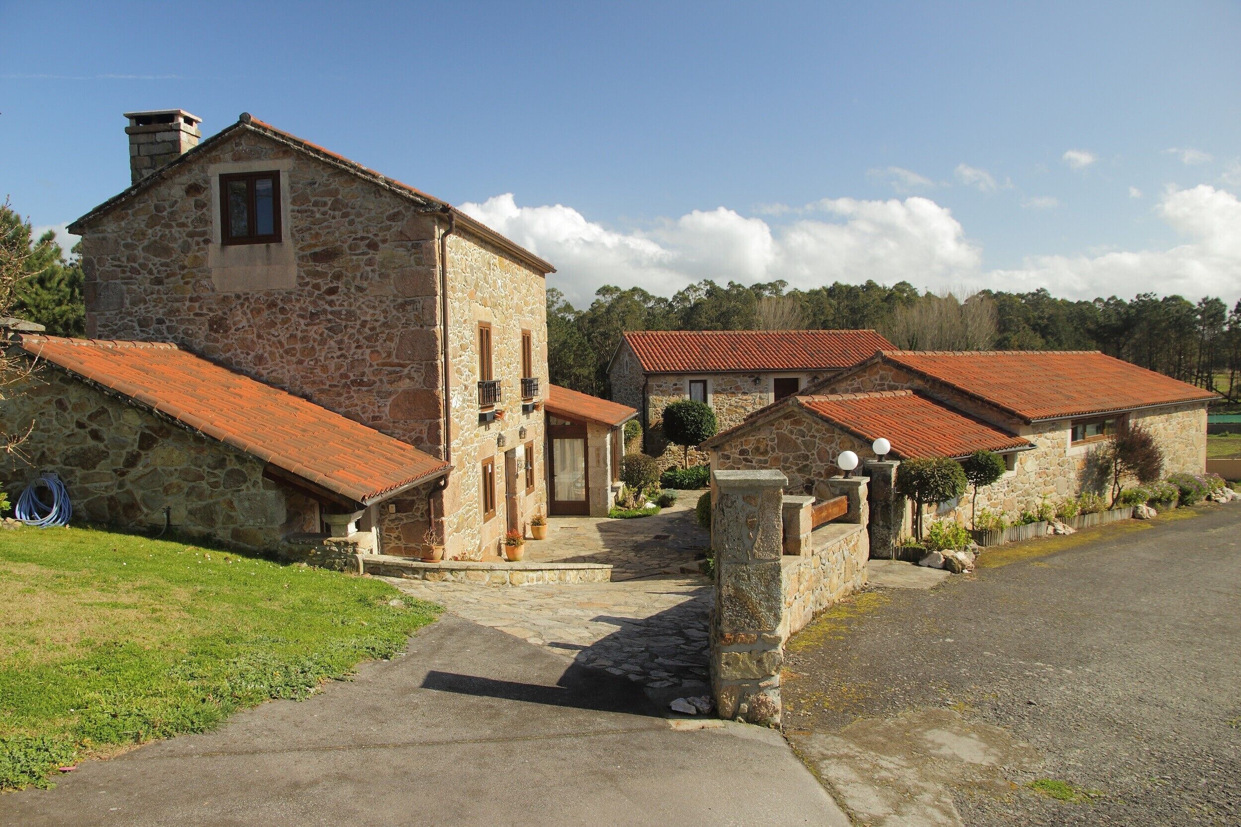 A stone building with a red-tiled roof, a stone entrance, and a paved driveway.