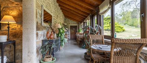A covered patio with stone walls, wooden ceiling, wicker furniture, and potted plants.