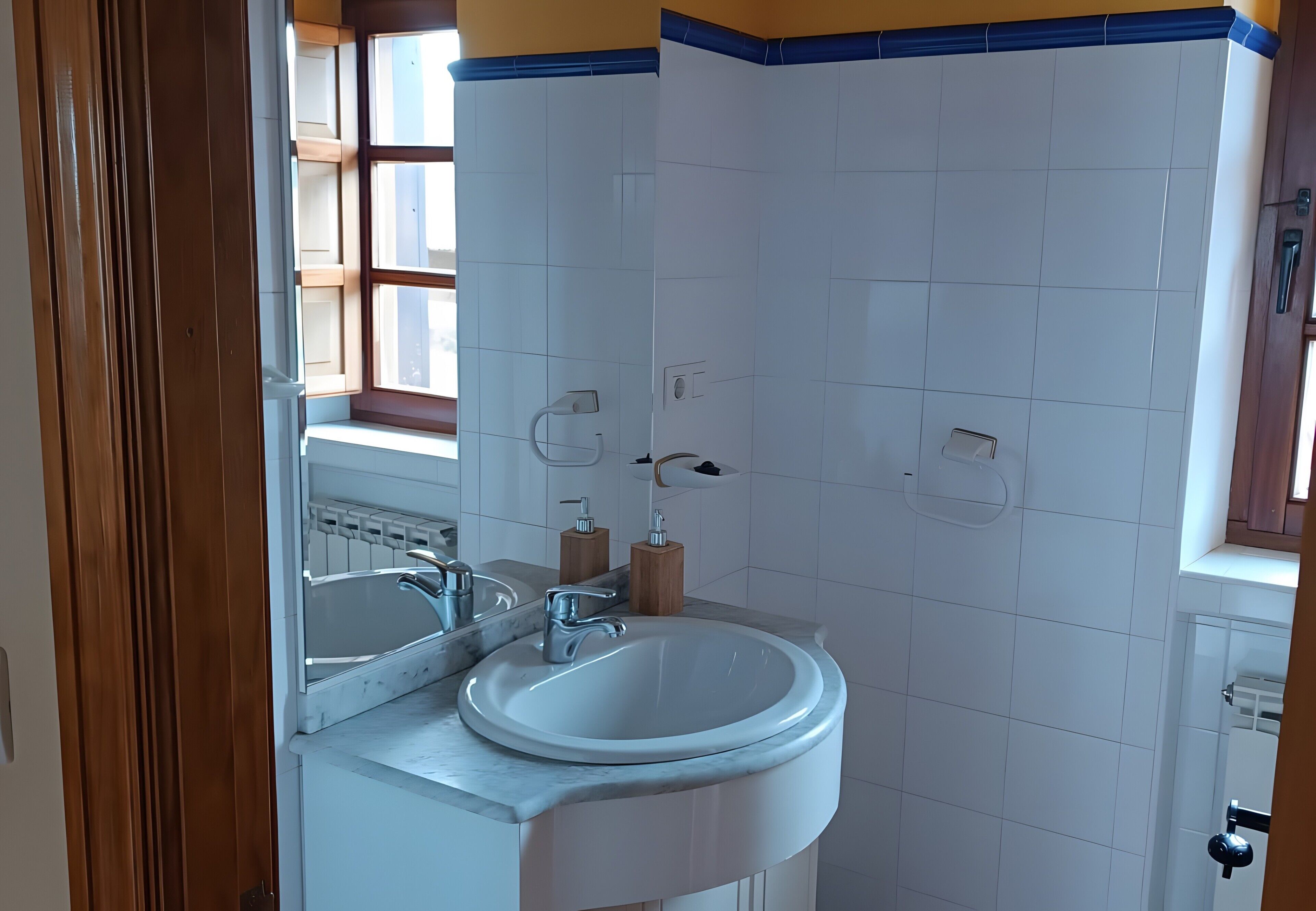 Baño con lavamanos blanco, un espejo y una ventana.