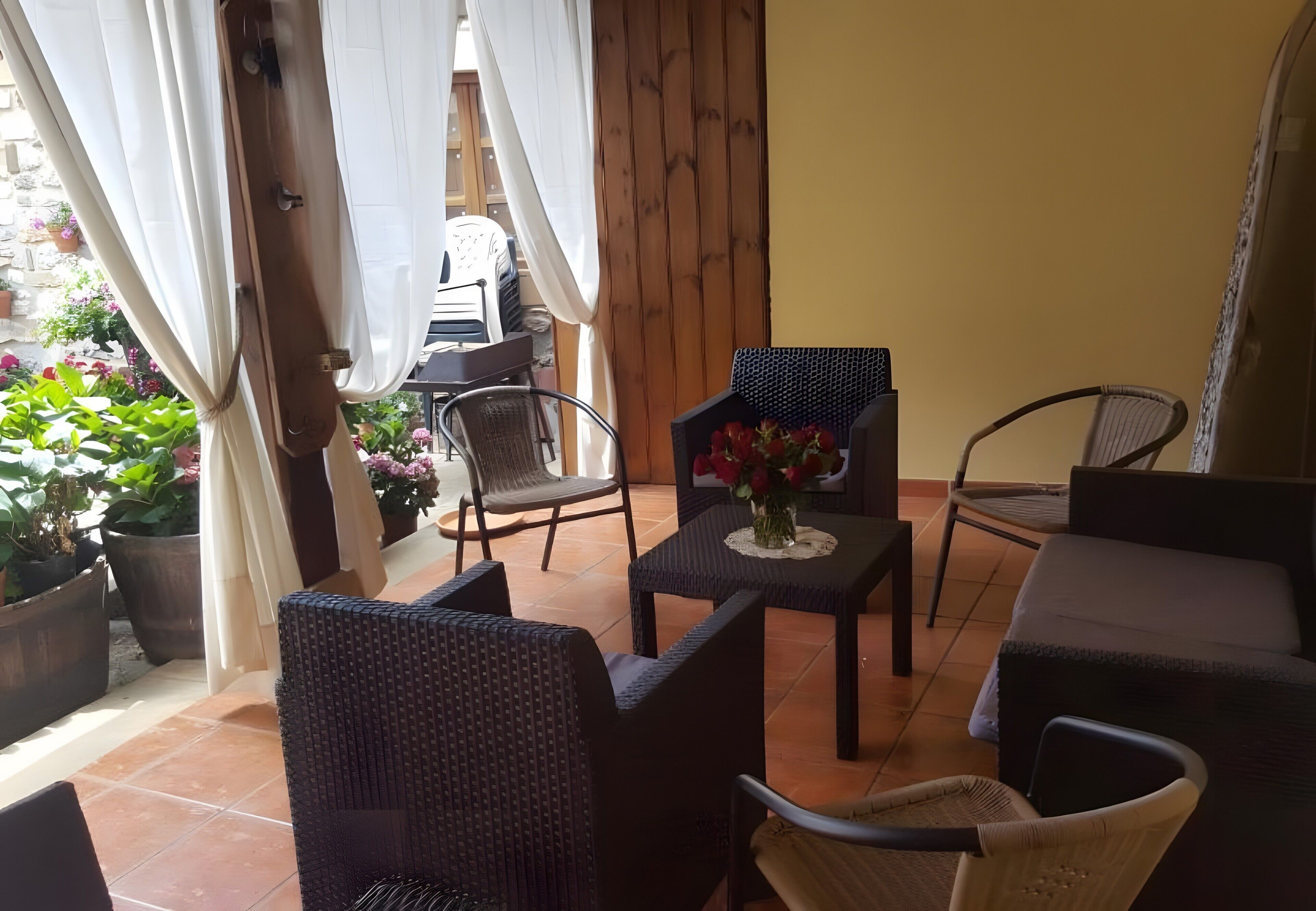 Un patio con mobiliario de mimbre, una mesita con un florero y vista al jardín.