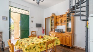 Un coin repas avec une table dressée pour deux personnes, un meuble en bois abritant un téléviseur et une porte verte donnant sur l’extérieur.