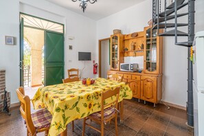 A dining area with a table set for two, a wooden cabinet with a television, and a green door leading outside.