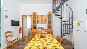 Une pièce compacte comprenant une table à manger, des chaises, un téléviseur, un four à micro-ondes et un escalier en colimaçon.