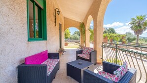 Une terrasse extérieure avec des meubles en osier, une fenêtre encadrée de verdure et une vue sur le jardin.