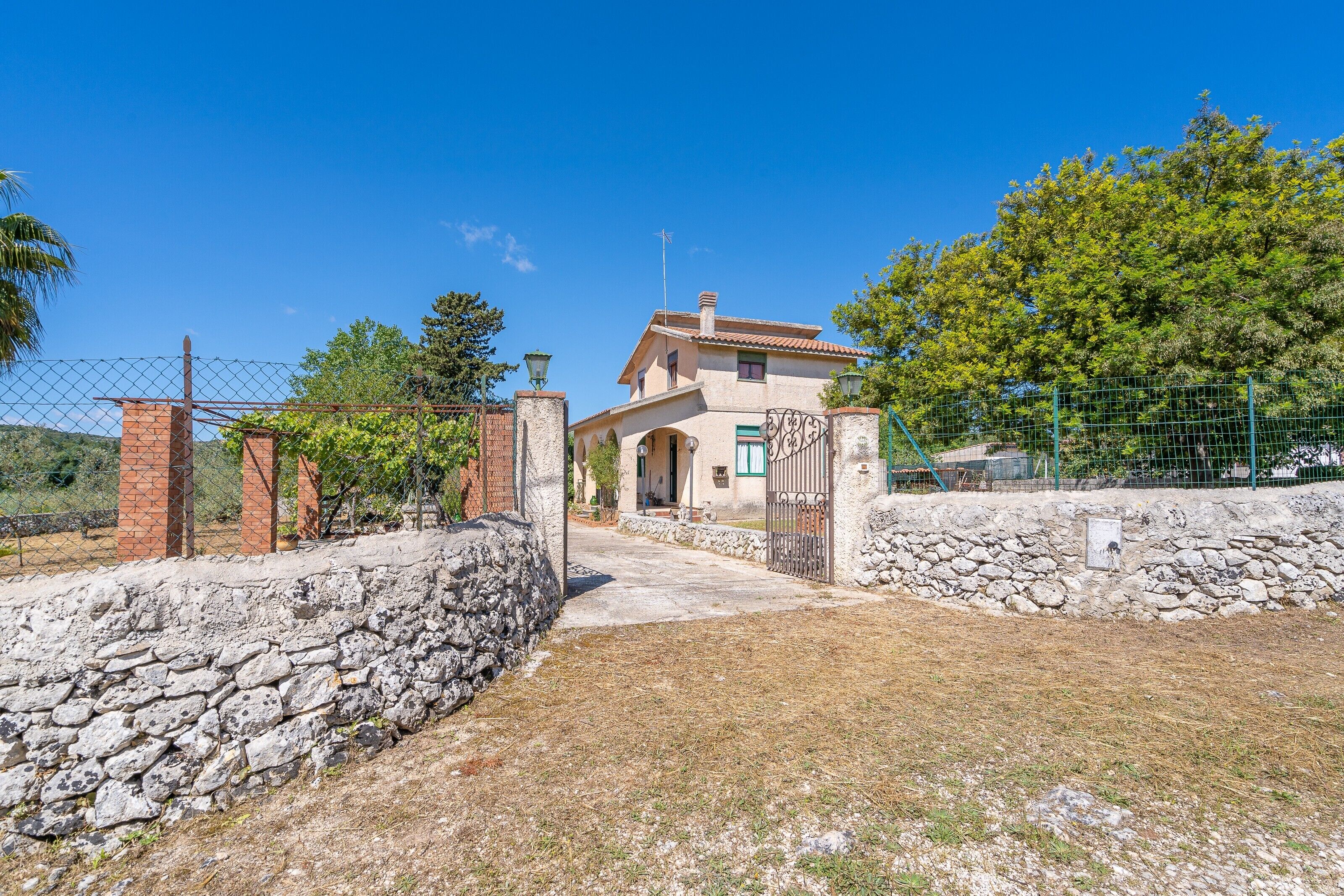 A house with a stone wall, a metal gate, and a clear sky.