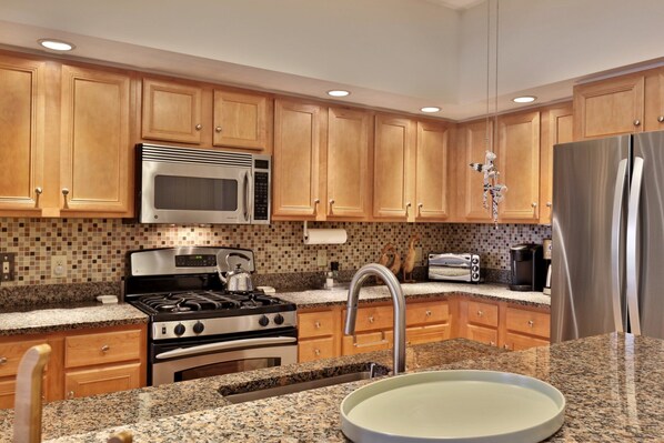 A modern kitchen with wooden cabinets, stainless steel appliances, granite countertops, and a stainless steel refrigerator.