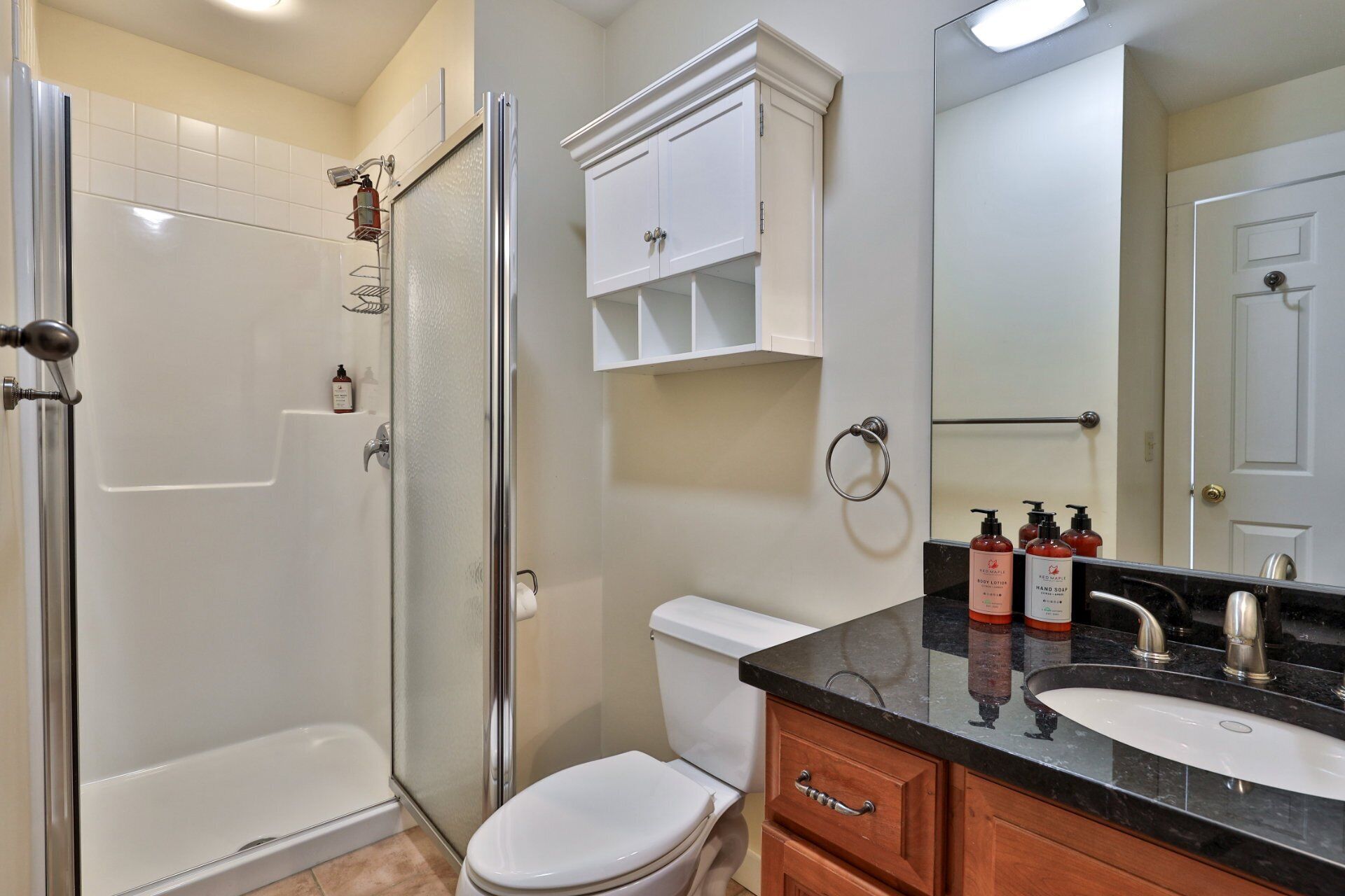 A bathroom with a glass-enclosed shower, a white toilet, a sink with a black countertop, and wooden cabinets.