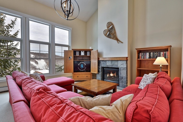 The living room includes red sectional seating, fireplace, tall windows, and mountain views.