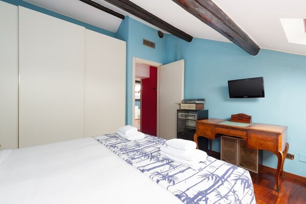A bedroom with a bed, a desk, a television, and a red door.