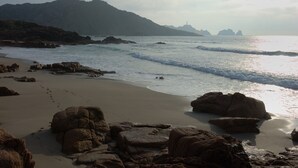 A beach with large rocks, waves, and distant mountains.