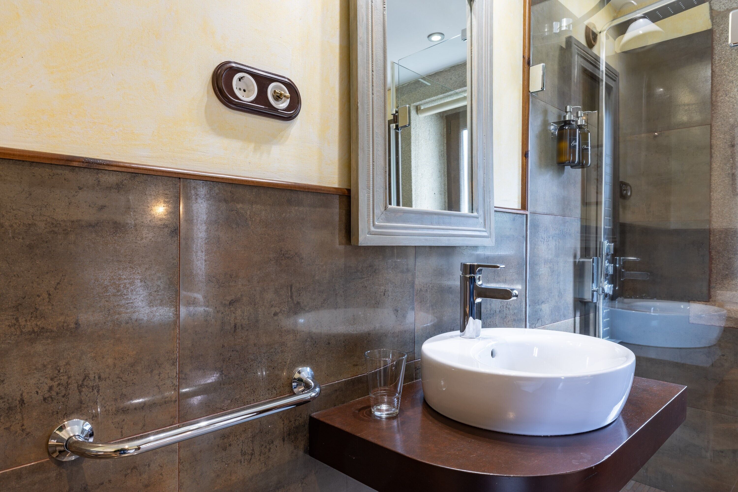 A bathroom with a white sink, a glass shower enclosure, and a handrail.