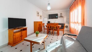 Una sala de estar con televisor, mueble de madera, mesa de comedor, sillas y sofá.