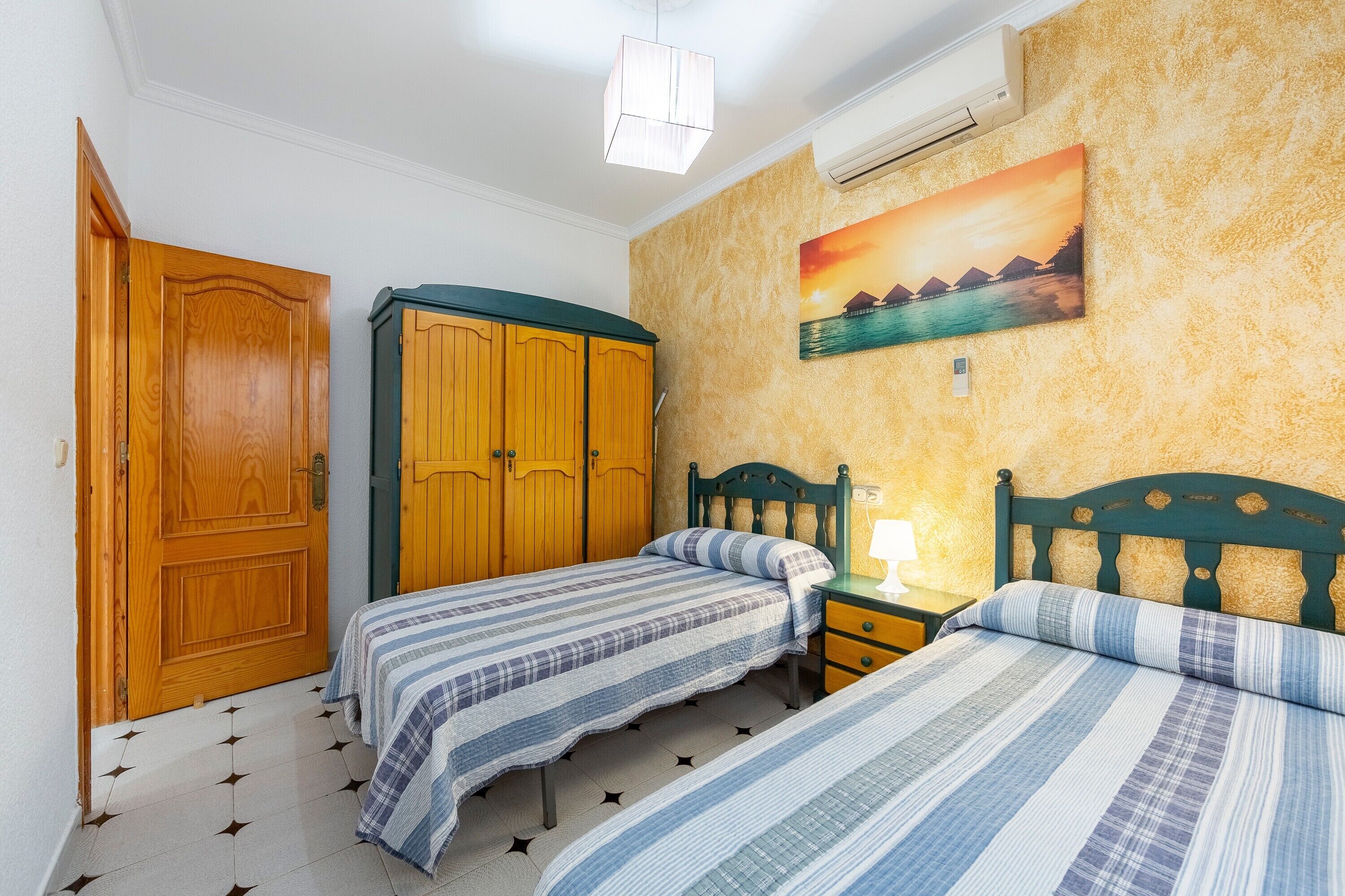 Un dormitorio con dos camas, un armario de madera y un cuadro en la pared.