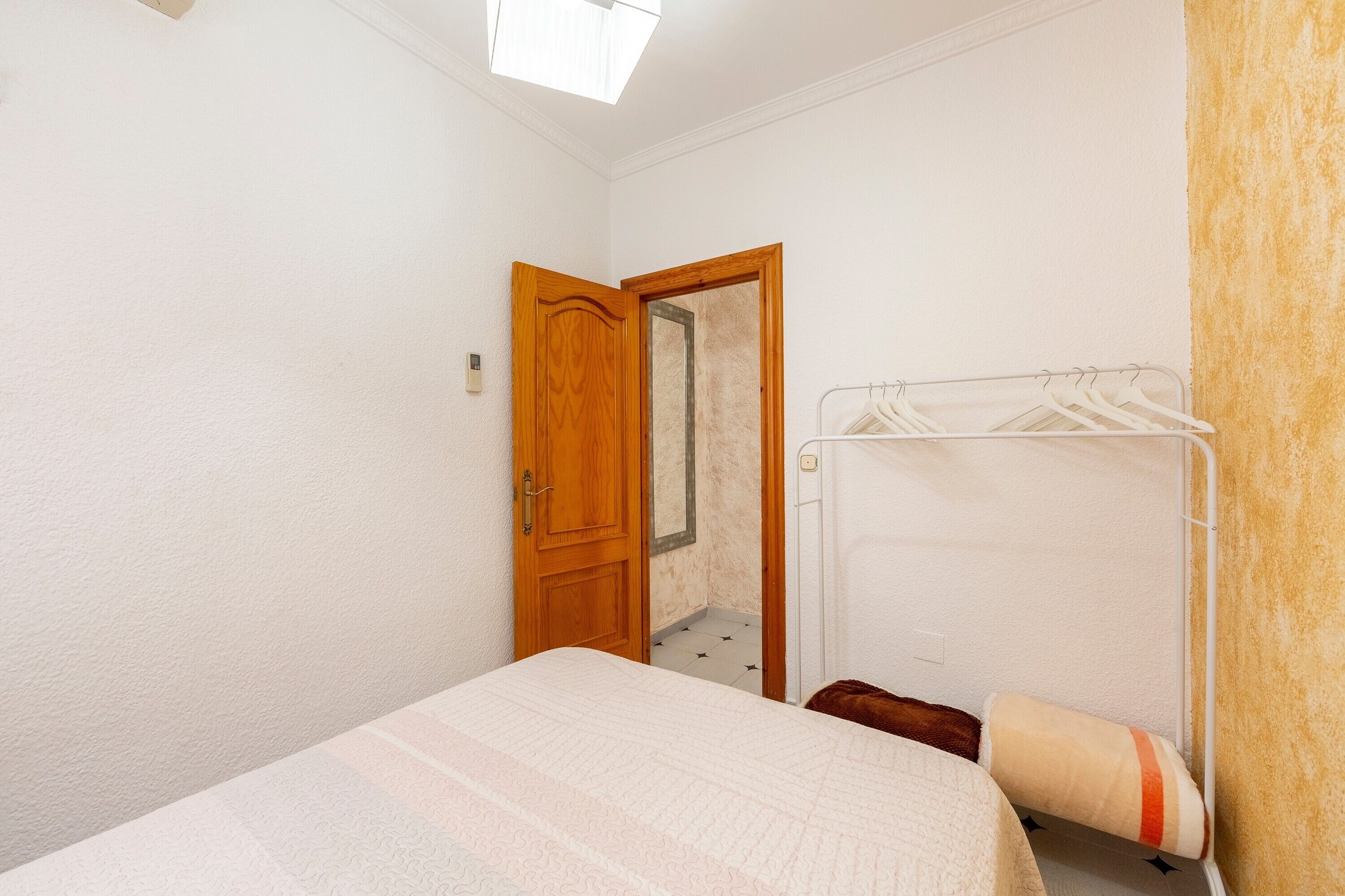 Une petite chambre avec un lit simple, une porte en bois, un miroir et un étendoir à linge.