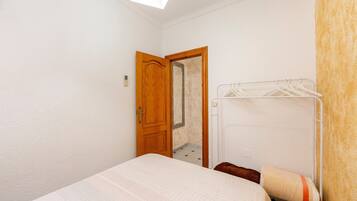 Une petite chambre avec un lit simple, une porte en bois, un miroir et un étendoir à linge.