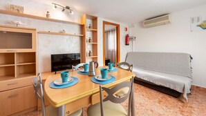 A compact room with a wooden dining table, chairs, a sofa, a TV, and shelves with various items. - Apartment 'La Noria 3' with Air Conditioning (Pozo de los frailes)