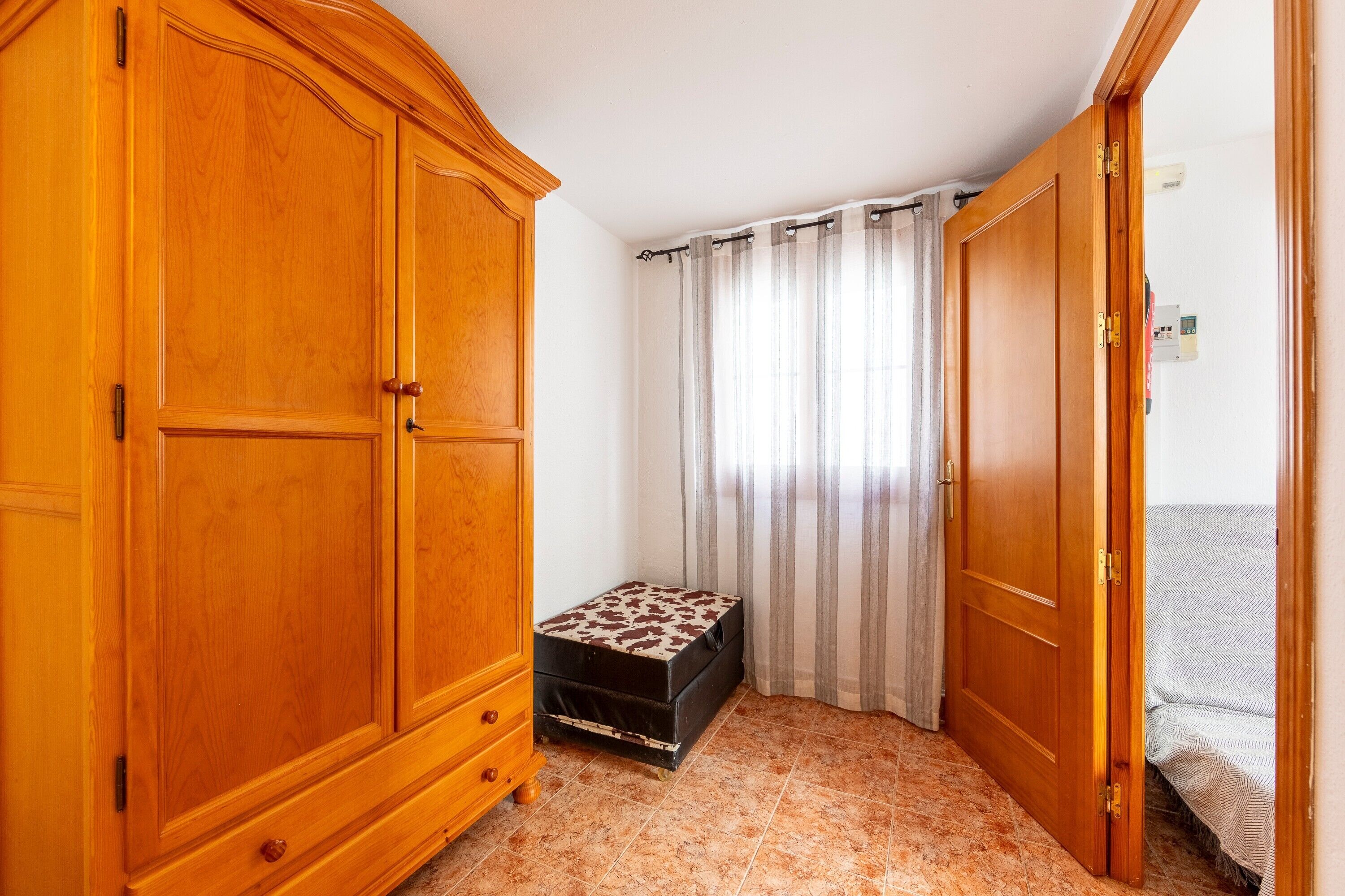 A room with a wardrobe, a bench, a curtain, and a bed.