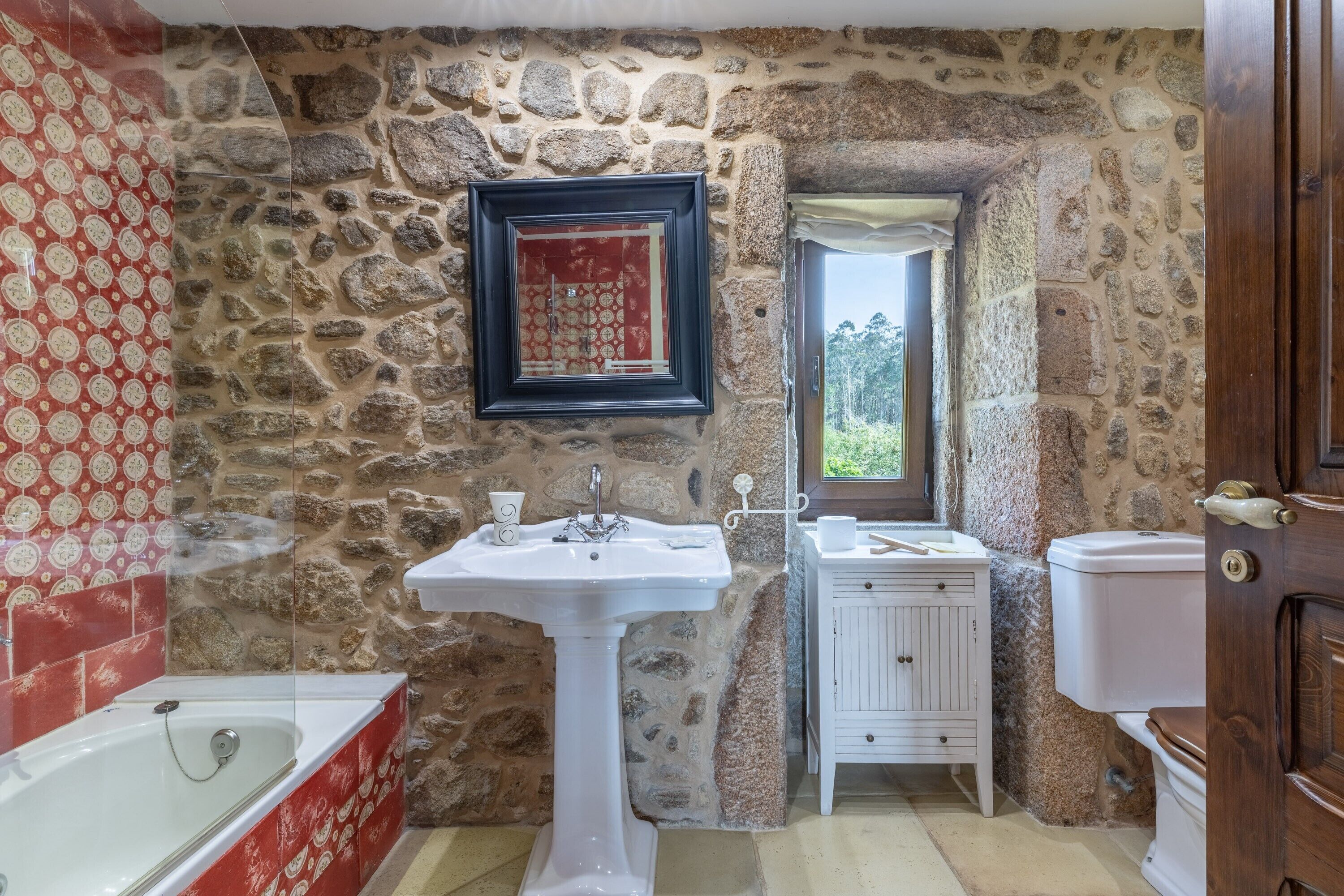 Een badkamer met een stenen muur, een wit wastafelmeubel, een wit toilet en een bad.