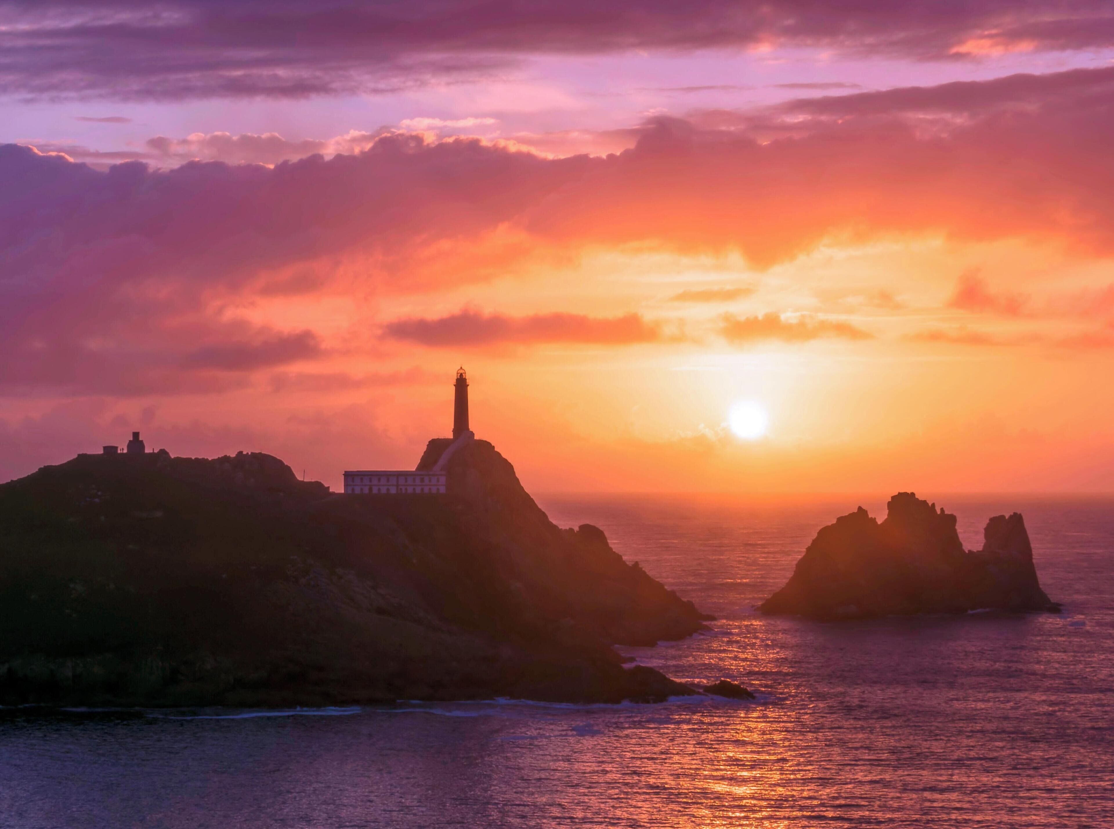 Un paysage côtier avec un phare et des formations rocheuses au coucher du soleil.