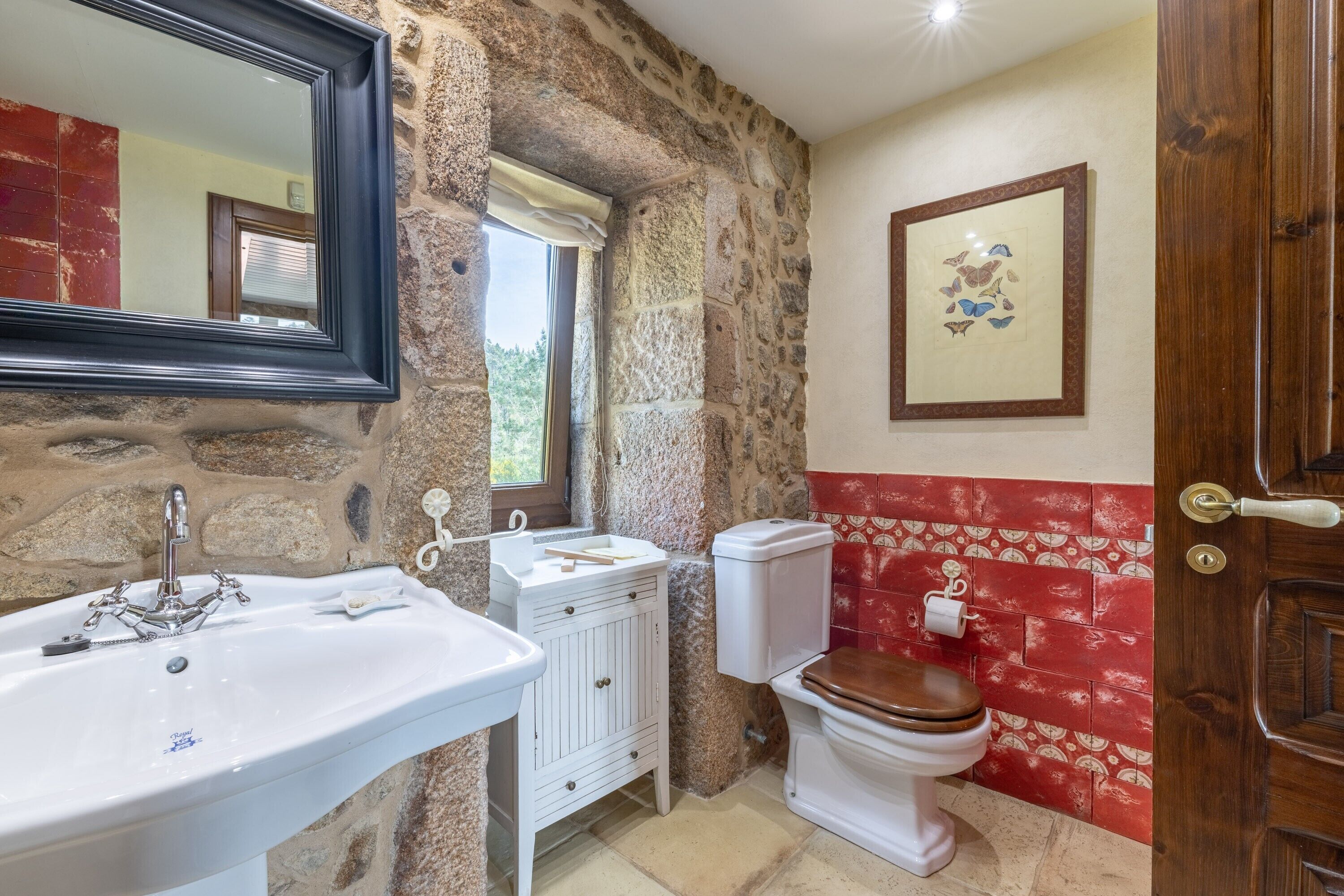 A bathroom with a stone wall, a white sink, a toilet, and a wooden door.