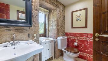 A bathroom with a stone wall, a white sink, a toilet, and a wooden door.