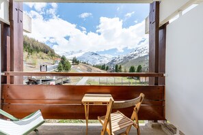 A wooden deck with a bench and a table, overlooking a mountain landscape with a road and a bridge.