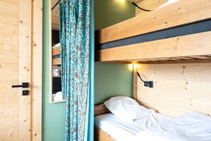 A bunk bed room with a mirror, a bedside table, and a curtain.