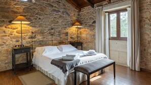 A stone-walled bedroom with a bed, two bedside lamps, a bench, and a window with curtains. - Bed and Breakfast 'Alcatraz' with Private Garden and Wi-Fi (Camariñas)