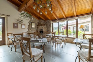 A dining area with stone walls, wooden ceiling beams, and hanging light fixtures. Tables and chairs are arranged for dining. - Double room 'Flamenco' (Camariñas)