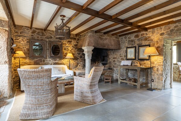 A stone-walled room with a fireplace, wicker furniture, and a ceiling with exposed beams.