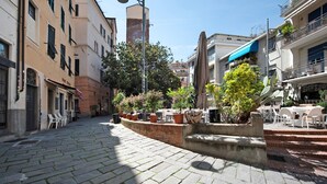 A cobblestone street with buildings on either side, outdoor seating, and potted plants.