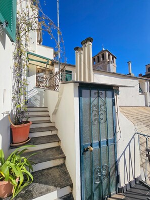 Eine Treppe führt zu einem Gebäude mit einer blauen Tür, einem Blumentopf und einem strahlend blauen Himmel.