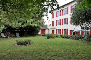 A building with red shutters, a well-maintained lawn, and a tree providing shade.