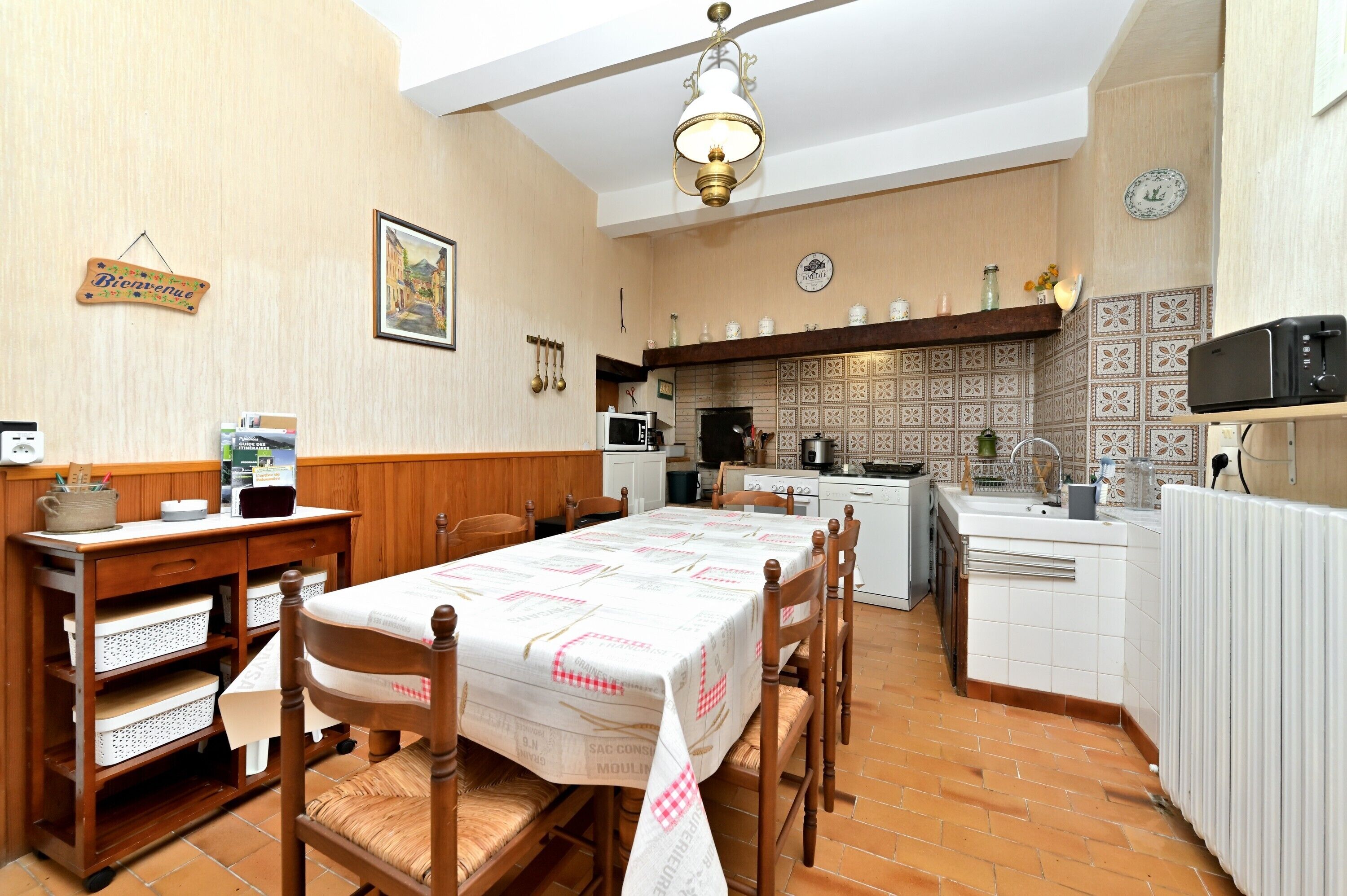 A dining area with a table set for four, a kitchen with a tiled backsplash, and a clock on the wall.