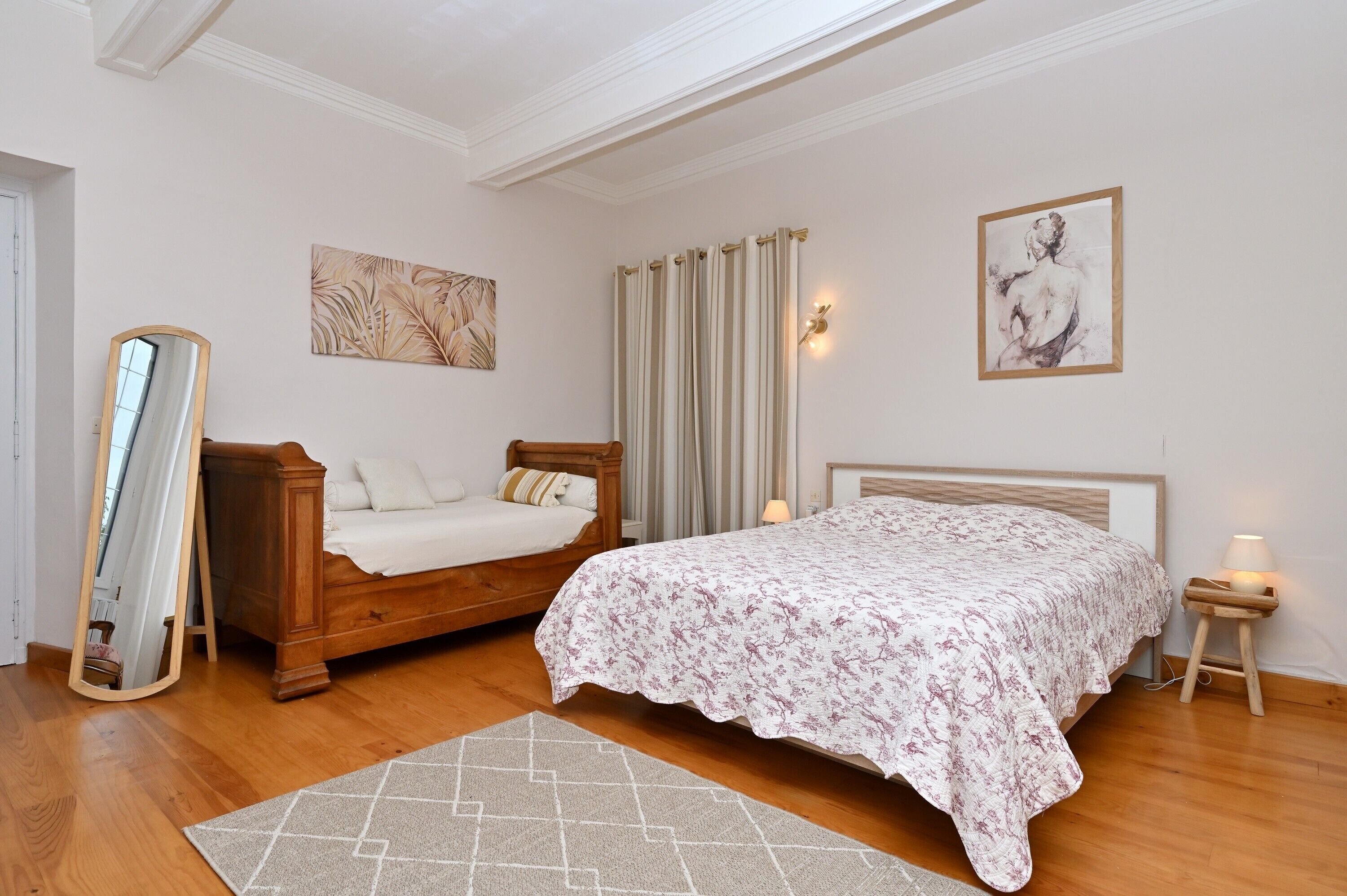 Un dormitorio con cama de madera, un espejo, una mesita de noche con lámpara y obras de arte en las paredes.
