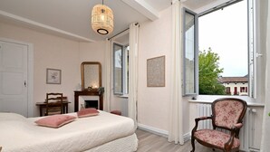 A bedroom with a bed, a chair, a mirror, and a window with a view. - Maison L'Arénoulat in Aspet – charm, garden & comfort in the heart of Comminges, near town & nature (Aspet)