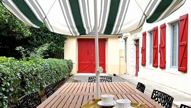 A wooden table with chairs, a tray with cups, a red door, and a striped awning. - Maison L'Arénoulat in Aspet – charm, garden & comfort in the heart of Comminges, near town & nature (Aspet)