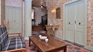 A room with a plaid sofa, a wooden table with decorative items, a staircase with a patterned wall, and a white door. - Maison L'Arénoulat in Aspet – charm, garden & comfort in the heart of Comminges, near town & nature (Aspet)