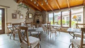 A dining area with stone walls, wooden ceiling beams, and hanging light fixtures. Tables and chairs are arranged for dining.