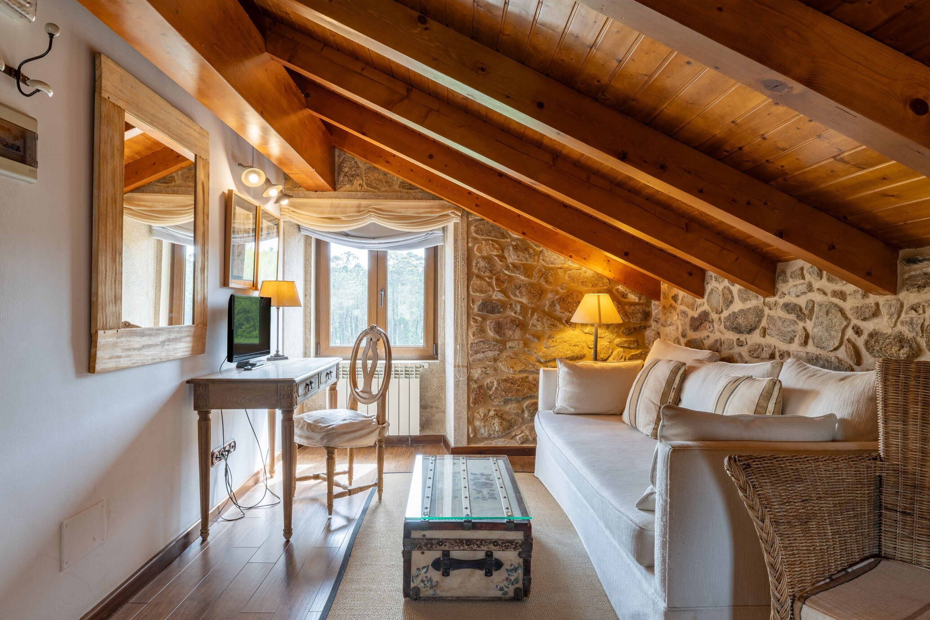 Ein gemütliches Schlafzimmer im Dachgeschoss mit freiliegenden Holzbalken, einer Steinwand, einem Bett, einem Schreibtisch und einem Stuhl.