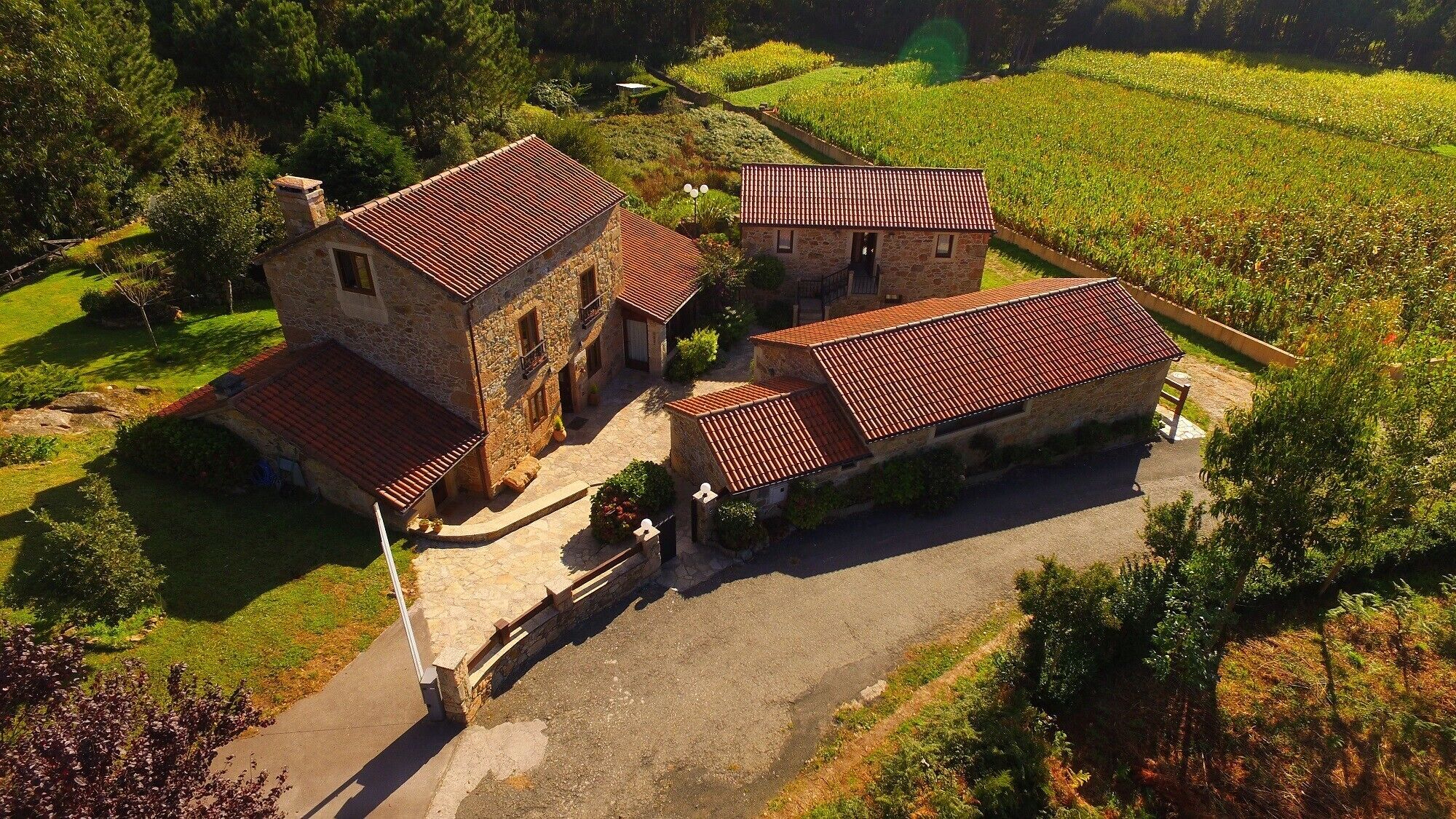 Un bâtiment en pierre, doté d’un toit en tuiles, entouré d’une allée pavée et d’une végétation luxuriante.