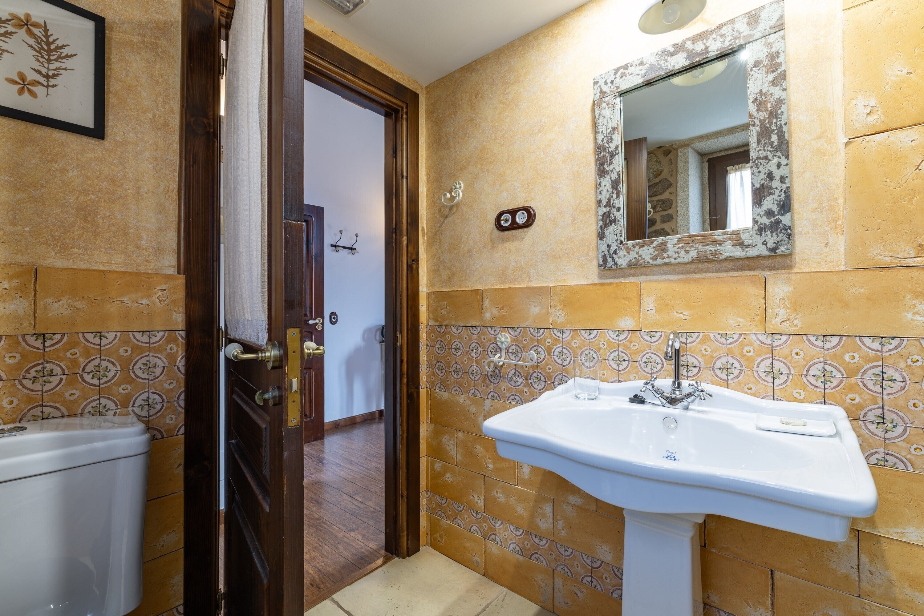 Een badkamer met toilet, wastafel, spiegel en wandtegels met een patroon.